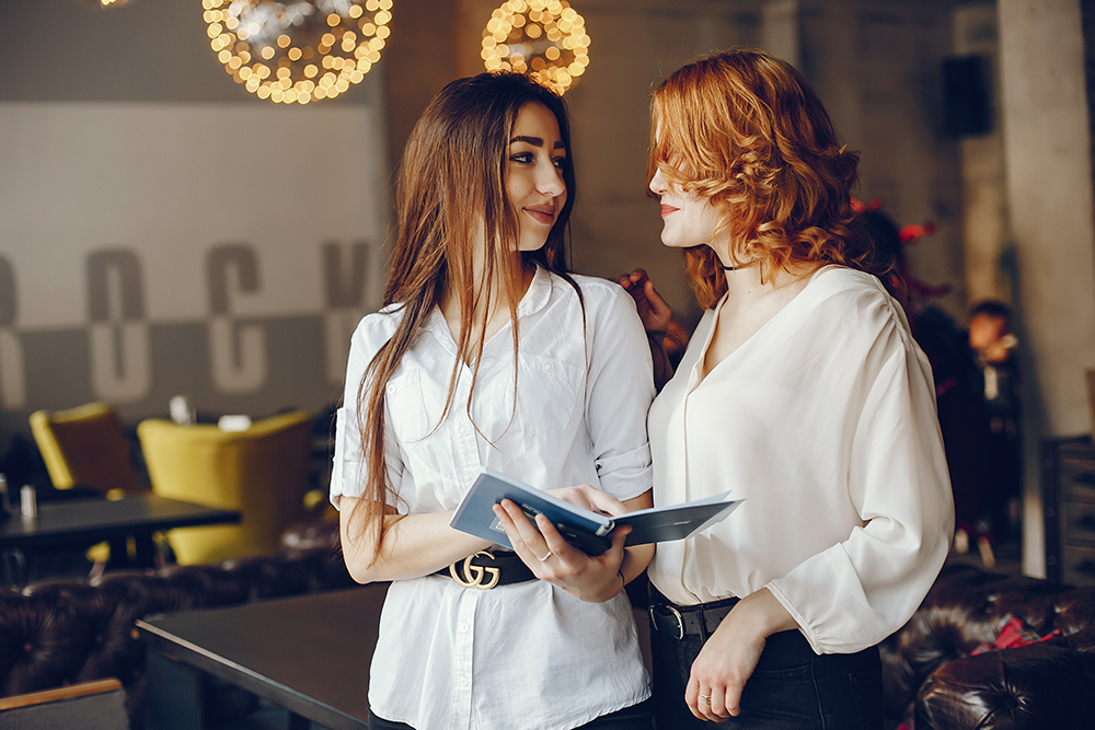 two businesswomen in a cafe two beautiful elegant girls in white shirts and black jackets standing in a restaurant and use notebooks